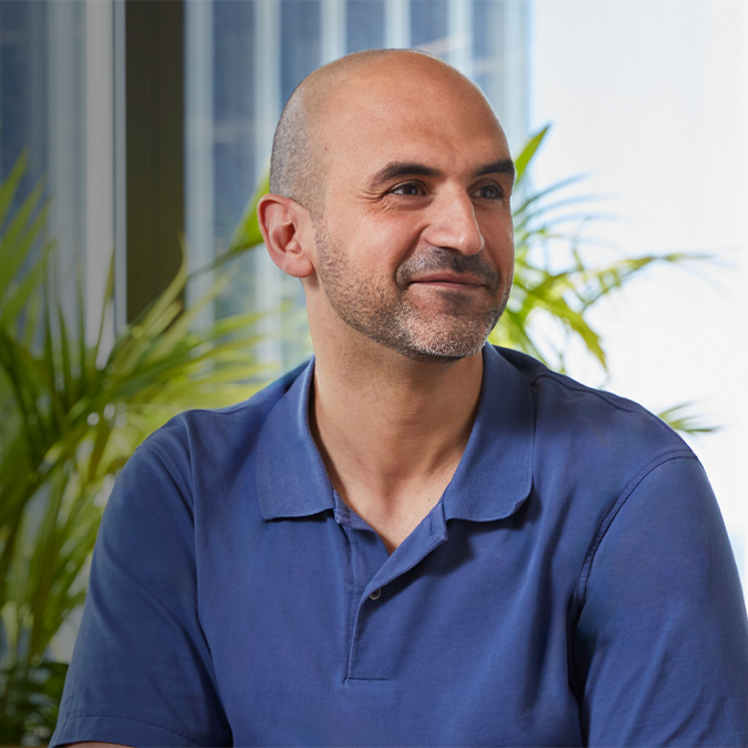 Ahmed 坐在室内，微笑看向自己的左侧，视线朝着镜头之外。