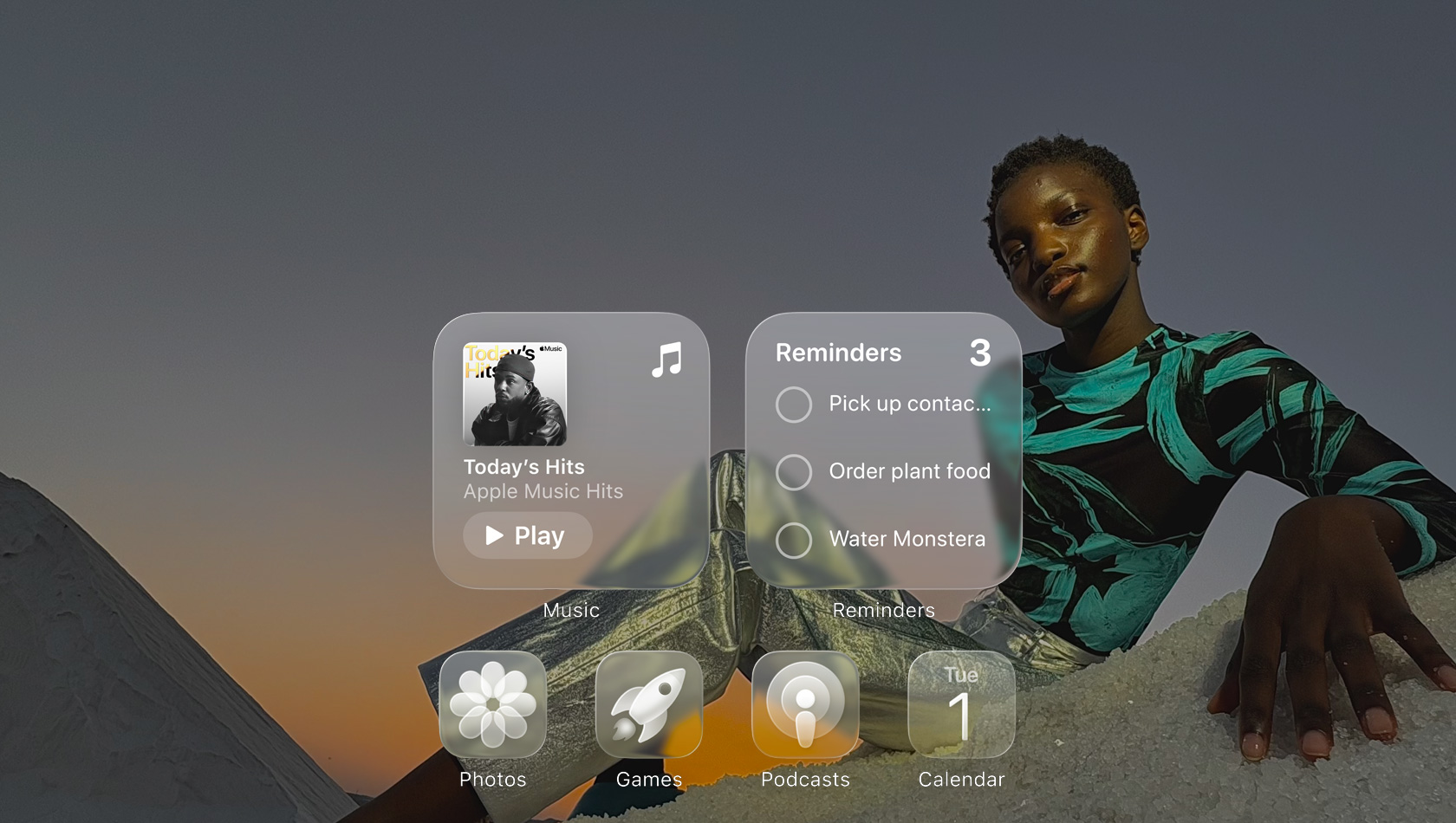 Displej v Liquid Glass designu s průsvitnými ikonami aplikací jako Apple Music, Připomínky, Fotky, Hry, Podcasty a FaceTime, přes které prosvítá tapeta