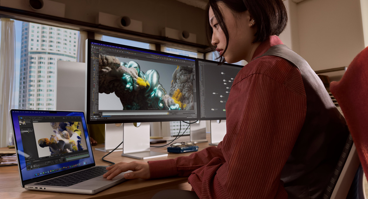 En person i et kontormiljø jobber på en MacBook-laptop som er koblet til Studio Display XDR via en Thunderbolt 5-port.