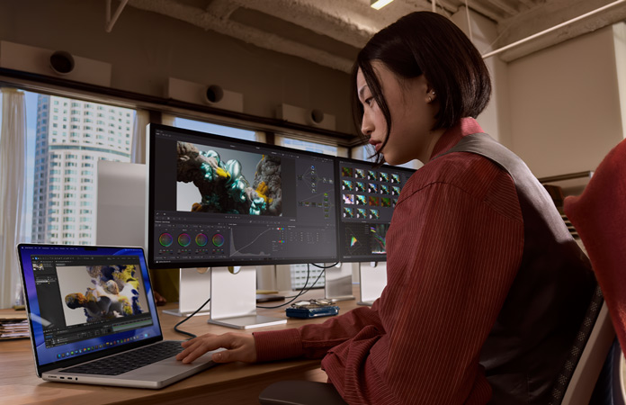 A person working in an office setting with MacBook Pro connected to Studio Display XDR