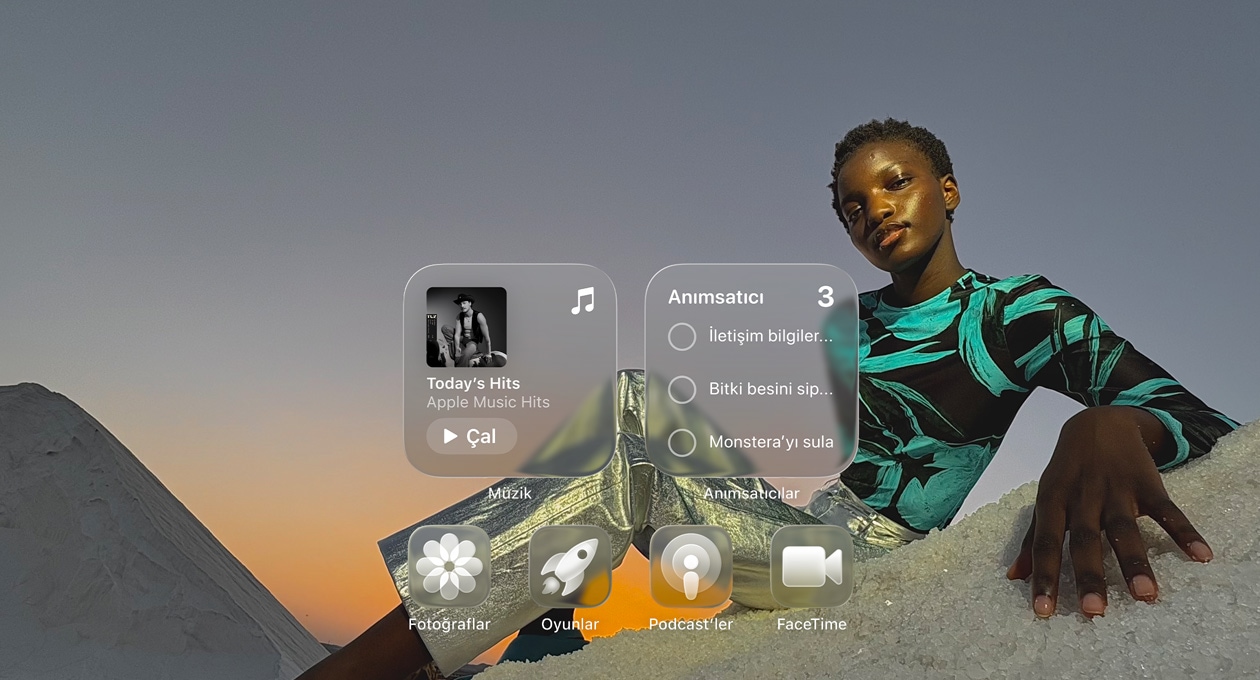 Liquid Glass ekranda yer alan Apple Music, Anımsatıcılar, Fotoğraflar, Oyunlar, Podcast’ler ve Takvim gibi şeffaf uygulama simgeleri duvar kağıdının renklerini yansıtıyor