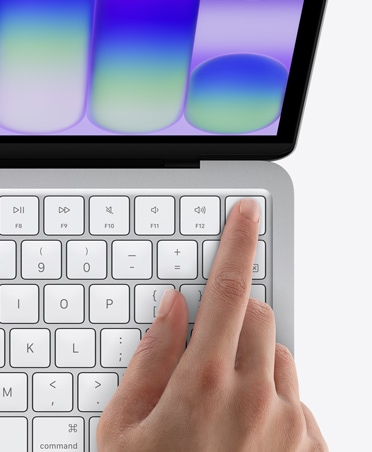 MacBook Neo сріблястого кольору, палець людини на датчику Touch ID у верхньому правому куті клавіатури