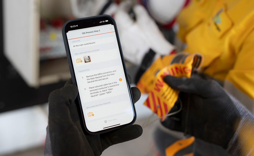 Hender holder en iPhone som viser instruksjoner for testing av en instrumenttavle og ordene «13C Process Step» på skjermen