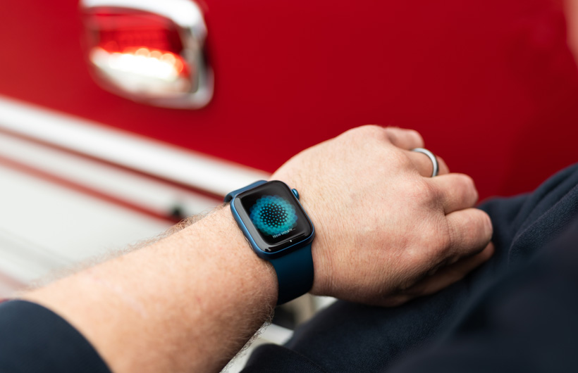 Ranteessa olevassa Apple Watchissa näkyvä viesti kehottaa hengittämään sisäänpäin, ja lähistöllä on paloauto