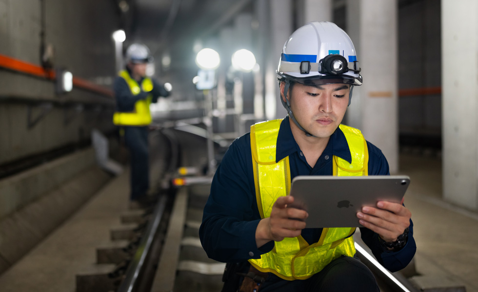 Un homme portant un gilet de sécurité et un casque regarde un iPad tout en effectuant des travaux d’entretien dans un tunnel du réseau de Tokyo Metro.