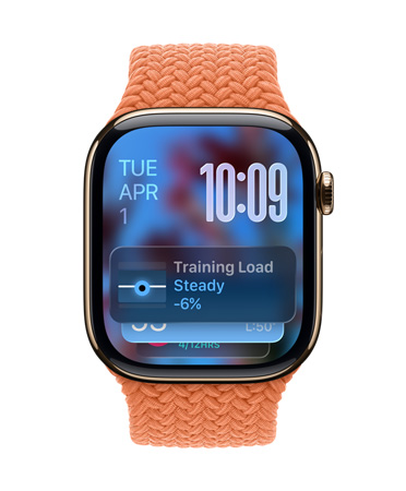 Une Apple Watch or rose avec un Bracelet tressé tangerine, le cadran affiche la date en haut à gauche, l’heure en chiffres superposés en haut à droite, le widget Charge d’entraînement en bas, le tout en Liquid Glass translucide