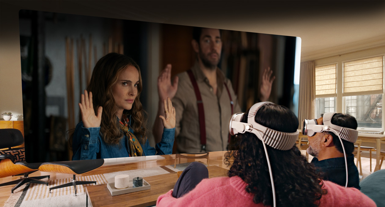 Two people both wearing Apple Vision Pro sit side by side on couch watching: Fountain of Youth movie, displayed on screen stretching across room