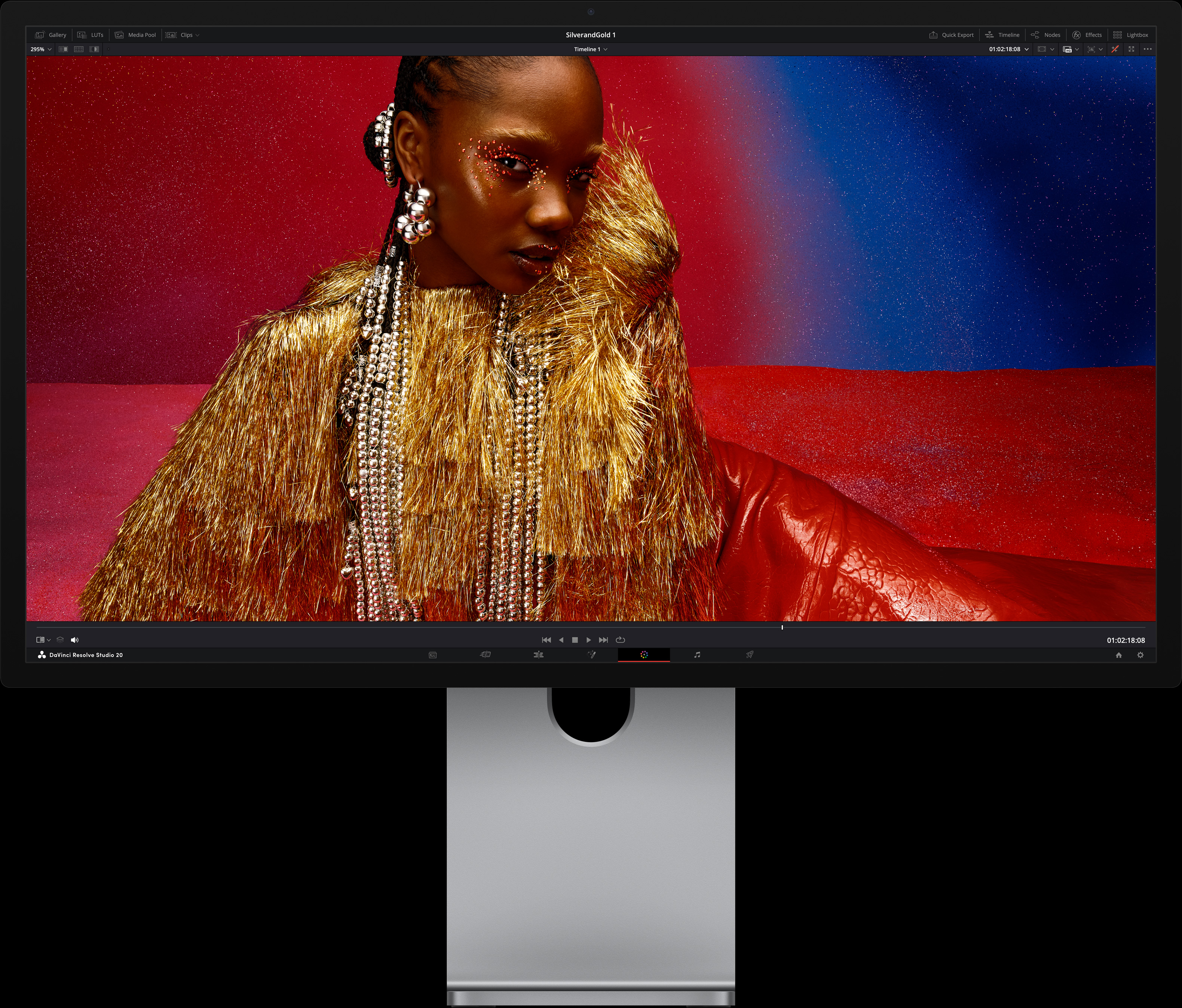 Eine Person in einem leuchtend roten Kleid und mit übergrossen metallischen Accessoires sitzt vor einem blau-roten Hintergrund, um die Bildqualität des Studio Display XDR zu demonstrieren